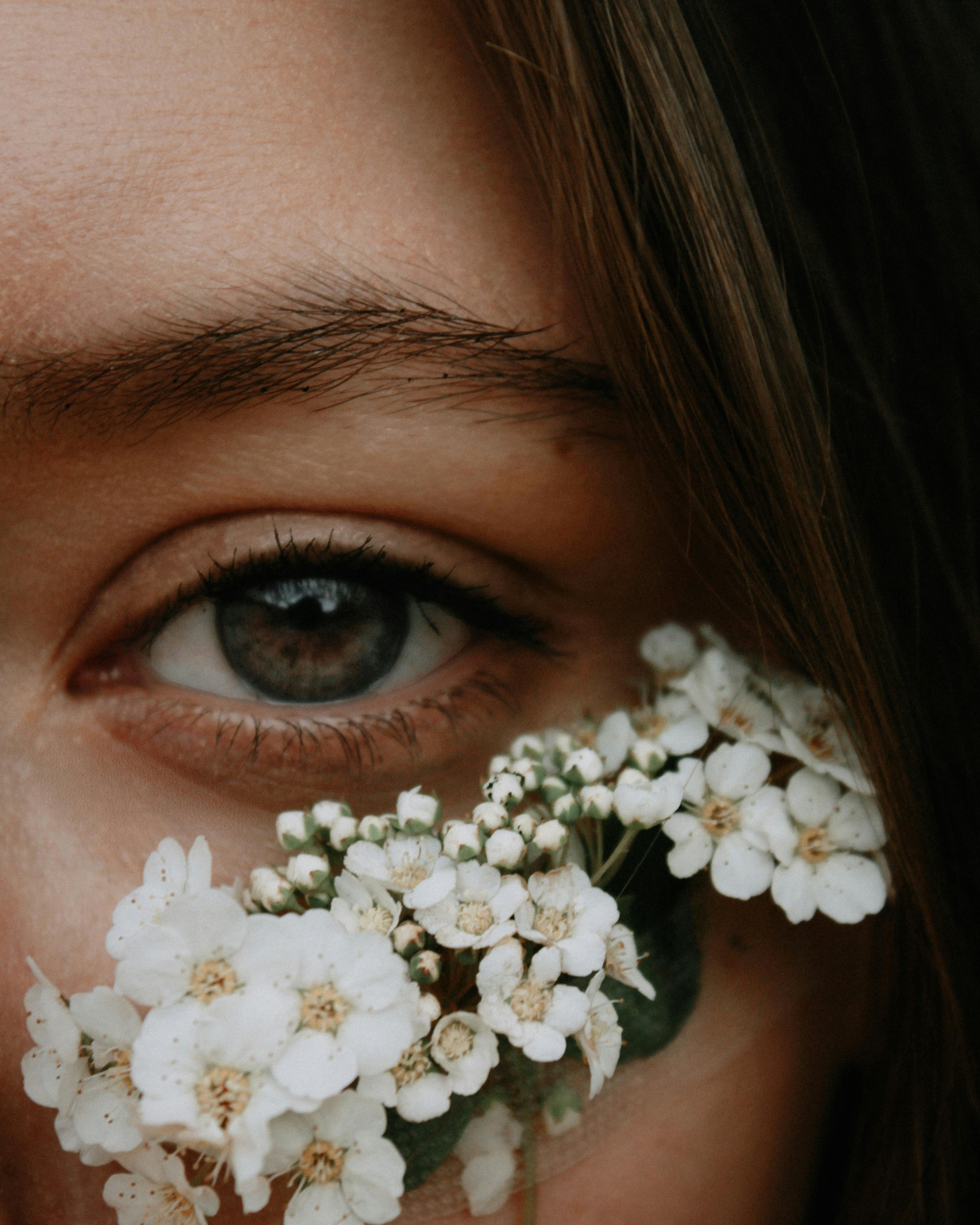 A close-up of an eye with delicate white flowers nearby, creating a serene composition.