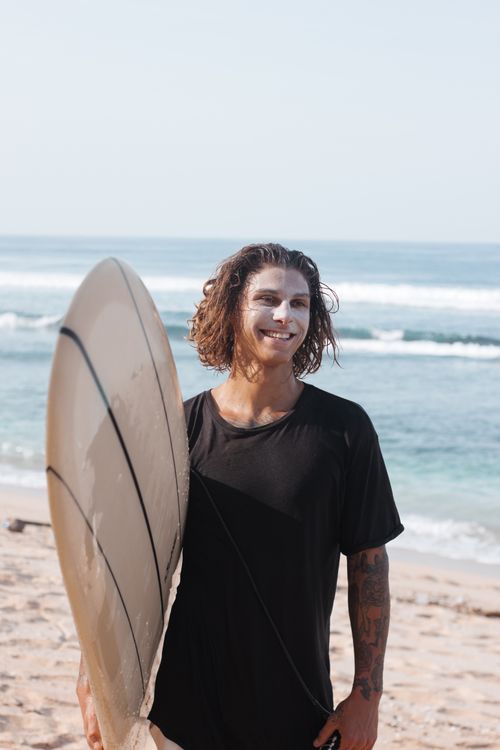 Free Happy man with surfboard on sunny beach day, enjoying summer vibes. Stock Photo