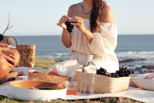 Free A woman enjoys a serene picnic by the beach with fruits and a woven basket. Stock Photo