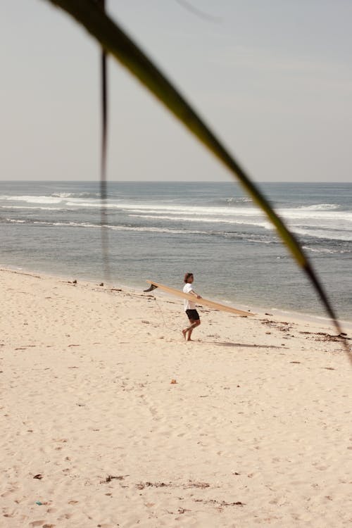 A Man Walking on the Beach Sand while Carrying Surfboard