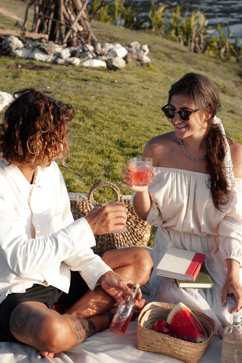 Free Couple enjoying a cheerful picnic outdoors, holding drinks and smiling. Stock Photo
