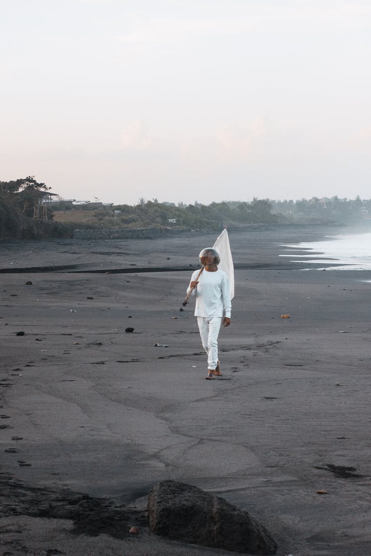 A Person Walking On The Beach Sand While Carrying A Flag