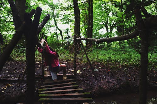 Девушка в розовой куртке на деревянном мосту в лесу