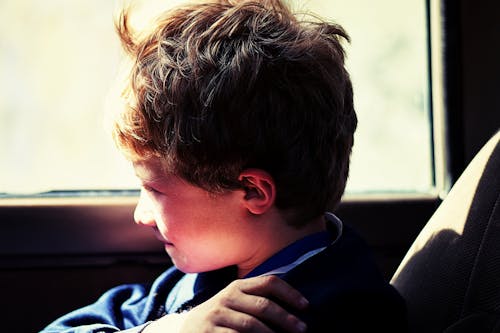 Boy in Blue Jacket Sitting Next to Vehicle Window