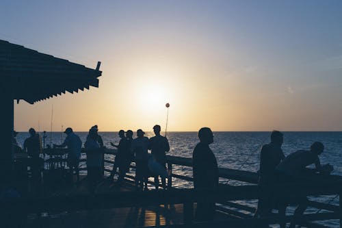 水域の近くの人々のシルエットに沈む夕日