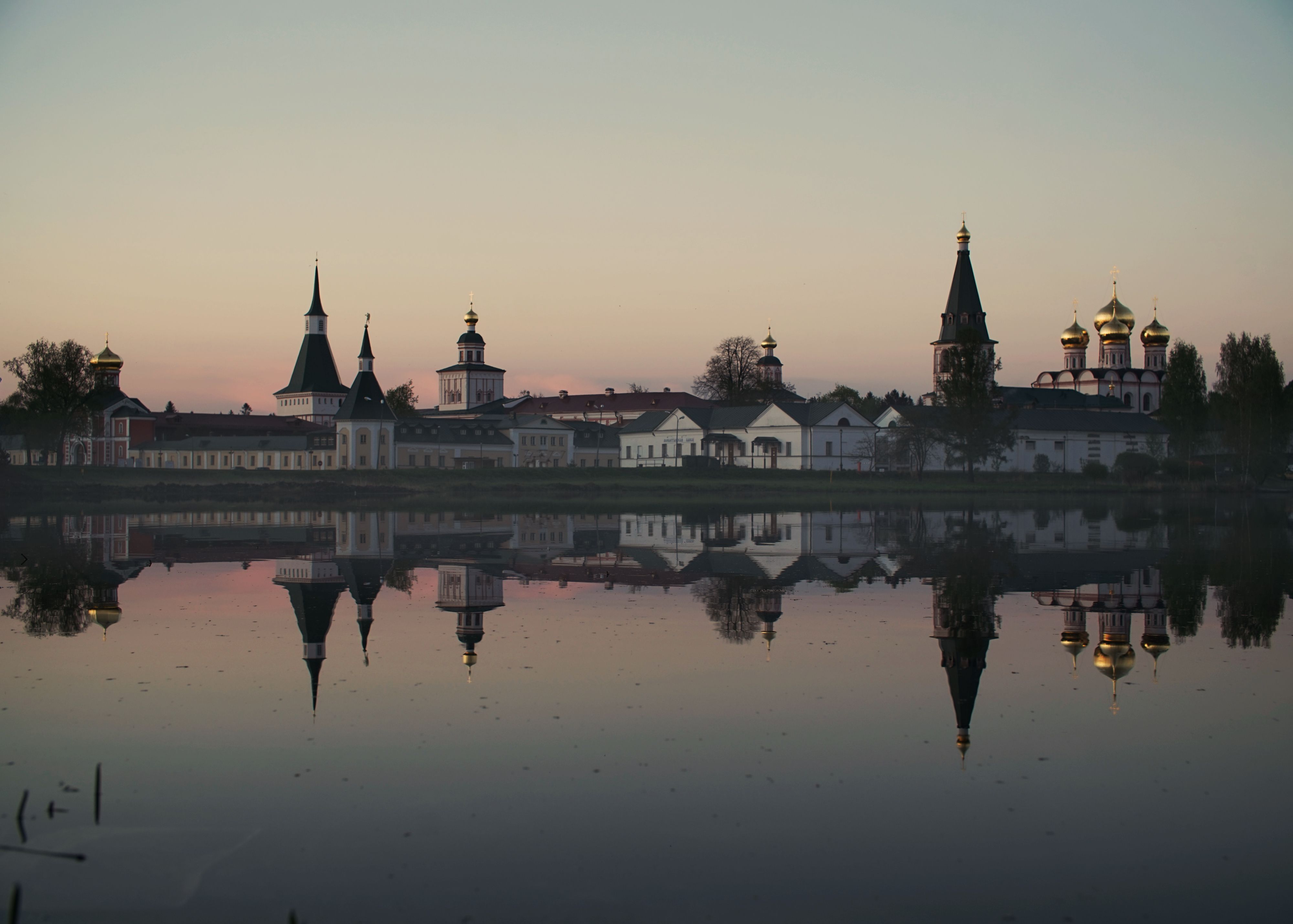 A tranquil sunset view of a monastery with reflections on a calm lake.