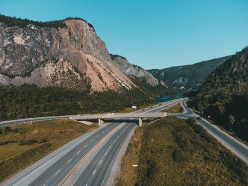 Free Aerial view of a highway passing through mountainous landscape under a clear blue sky. Stock Photo