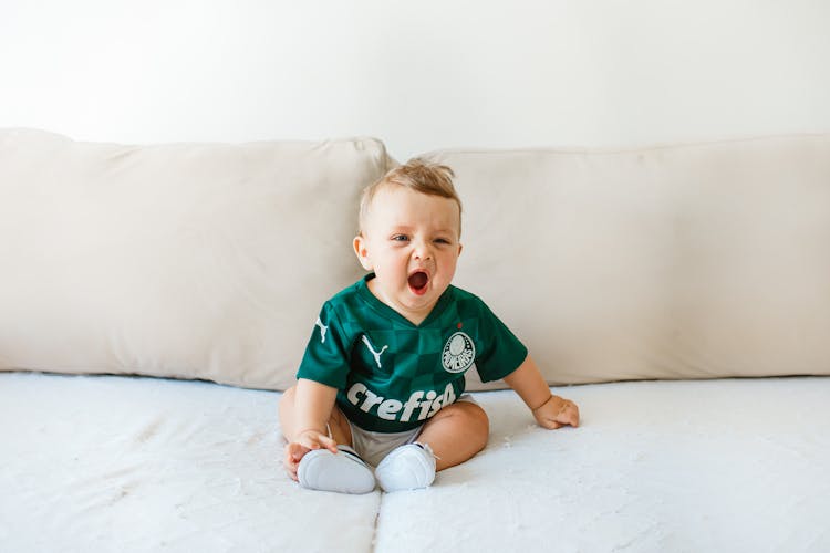 A Cute Baby Boy Yawning While Sitting On The Couch