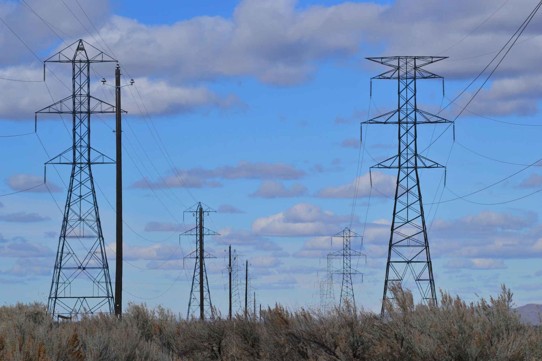 Power lines stretch across a rural landscape under a bright blue sky, emphasizing energy distribution.
