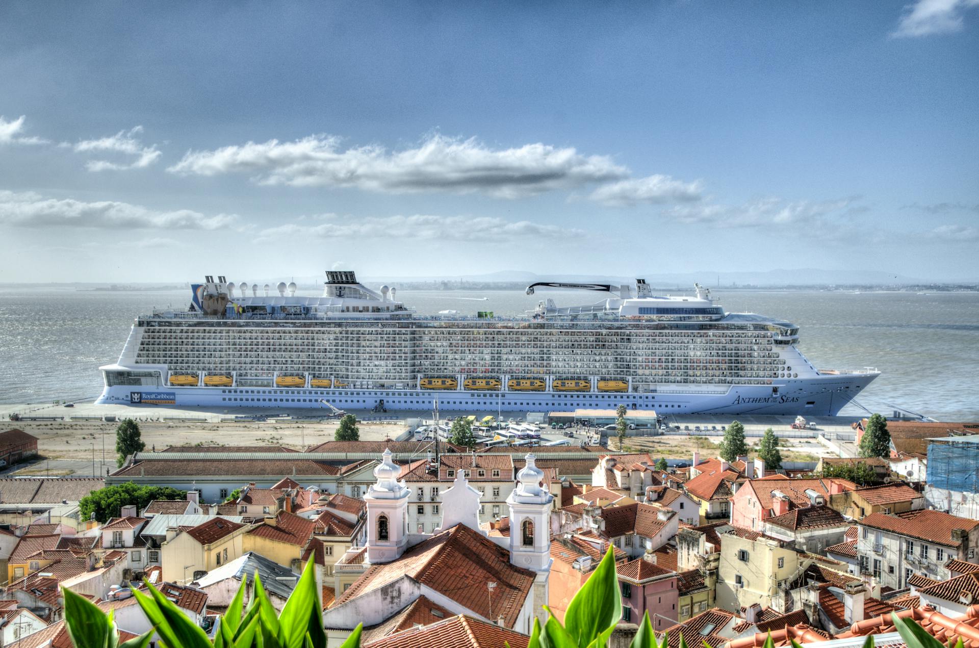 A luxurious cruise ship docked near a picturesque coastal town with vibrant architecture.