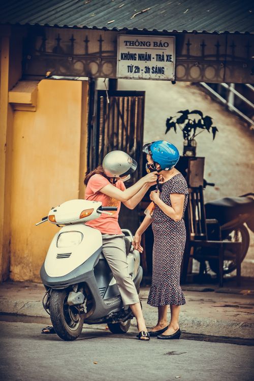 Free Two women wearing helmets interacting beside a scooter on a city street. Stock Photo
