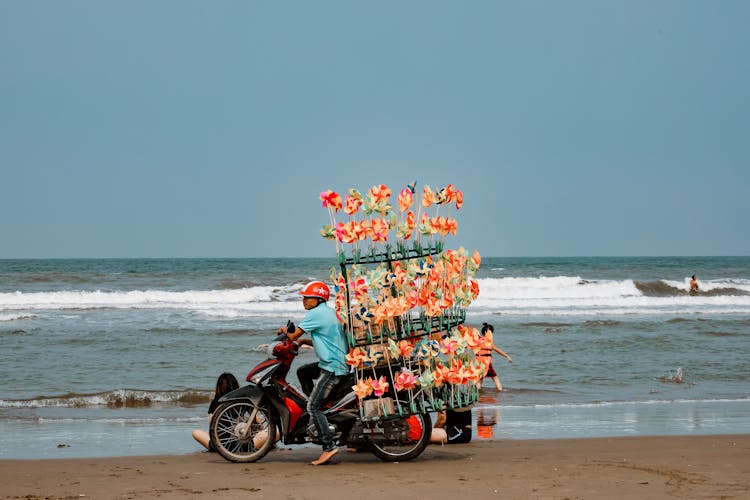 A Man Riding A Motorcycle On The Beach While Selling Pinwheels