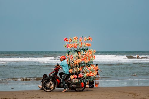 Free A vendor rides a motorcycle filled with colorful pinwheels along a vibrant beach shore. Stock Photo