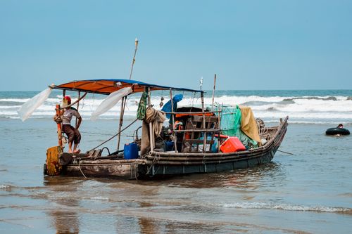 Free A traditional fishing boat with people navigating near the beach on a clear day. Stock Photo