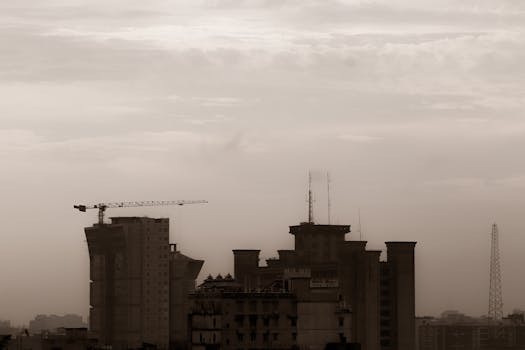 A city skyline featuring construction cranes and buildings in a sepia tone, creating a moody, urban atmosphere.