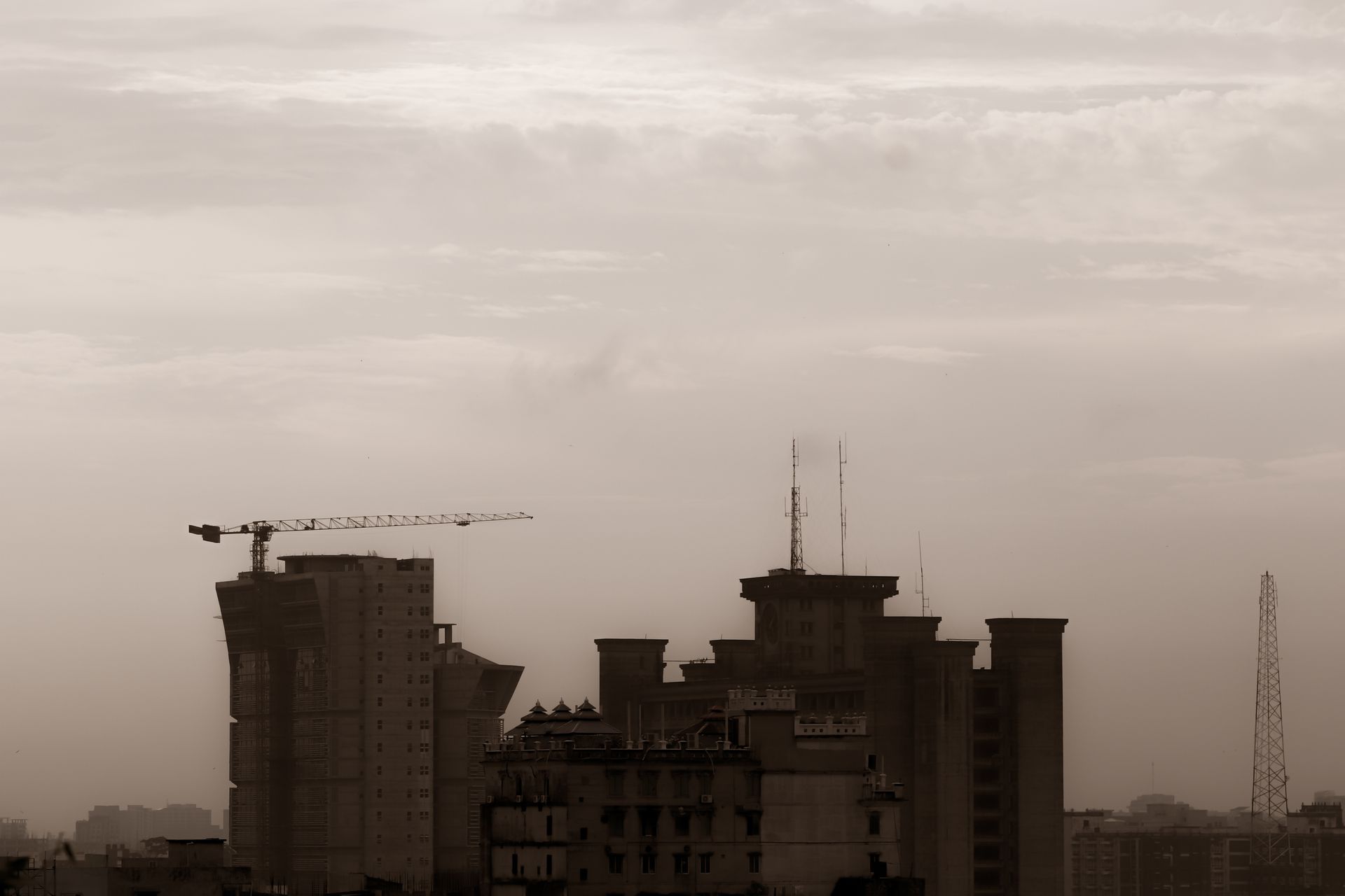A city skyline featuring construction cranes and buildings in a sepia tone, creating a moody, urban atmosphere.