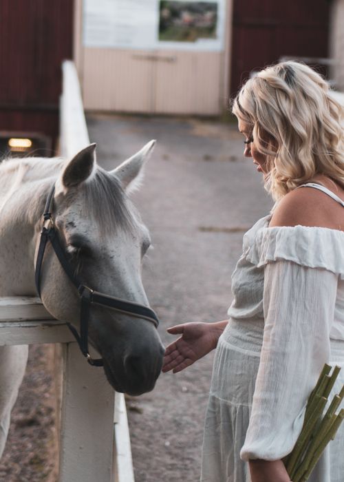 Free A woman gently interacts with a white horse at an outdoor stable. Stock Photo