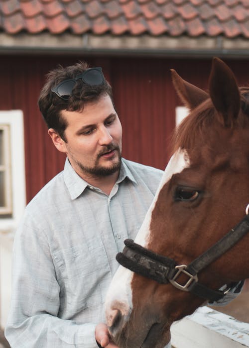 Photo of a Man in a White Long Sleeve Shirt Looking at a Horse