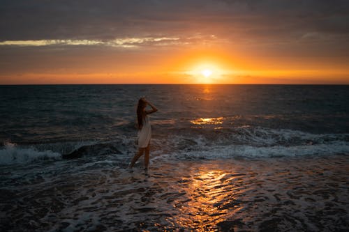 A Woman Walking on the Beach During Sunset