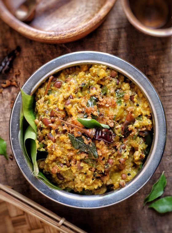 Steel bowl of lentil and rice khichdi topped with curry leaves, dried chili and coconut