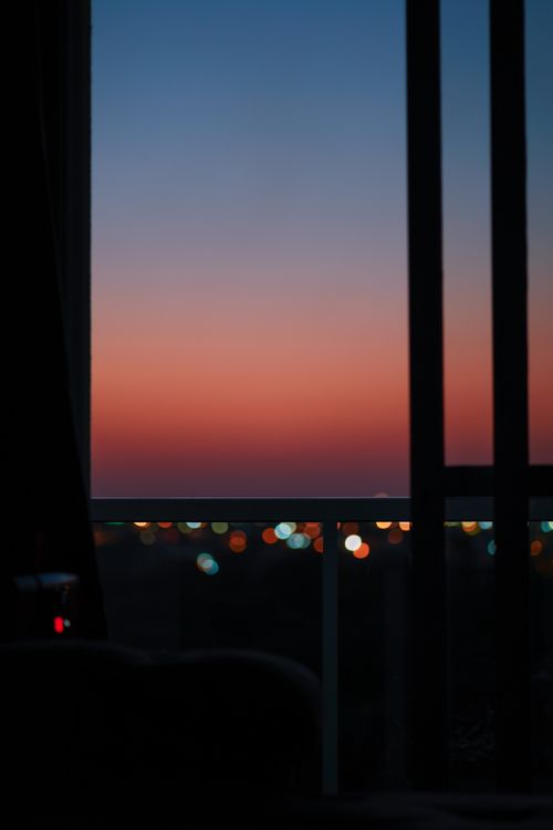 Free Capture of a vibrant sunset viewed from a balcony, featuring a bokeh cityscape. Stock Photo