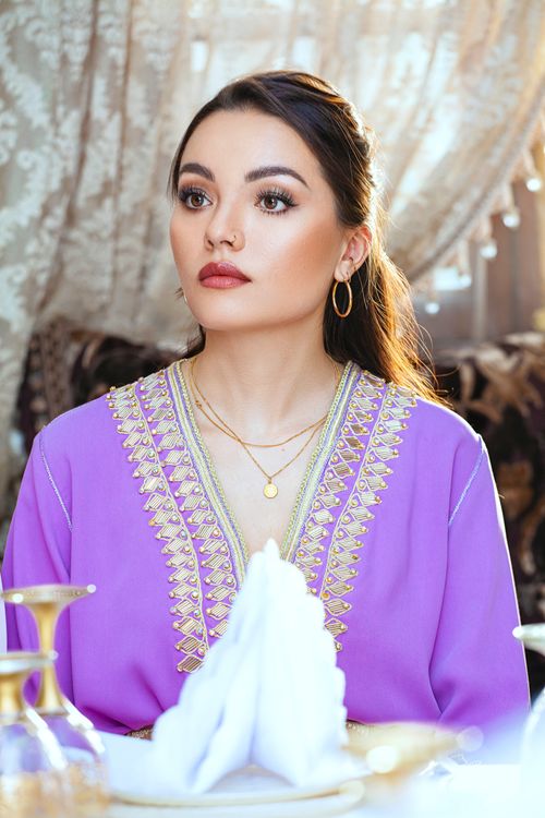 Free Portrait of an elegant woman in traditional attire, sitting indoors with decorative curtains. Stock Photo