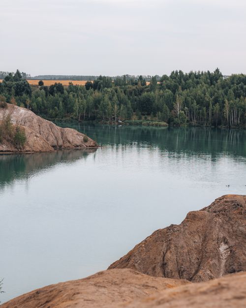 Free Peaceful natural lake surrounded by forest and rocky formations, ideal for nature lovers. Stock Photo