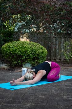 Woman in yoga pose on a mat outdoors in a serene garden setting