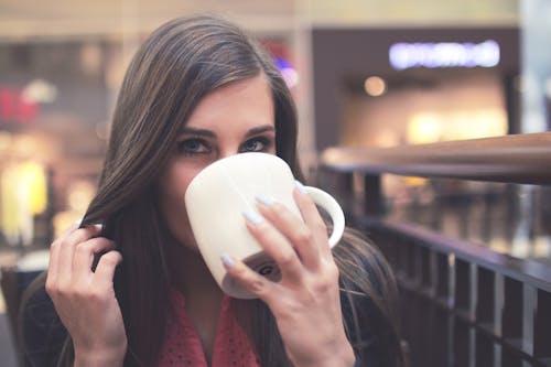 Woman in Black Mascara Drinking on White Ceramic Mug