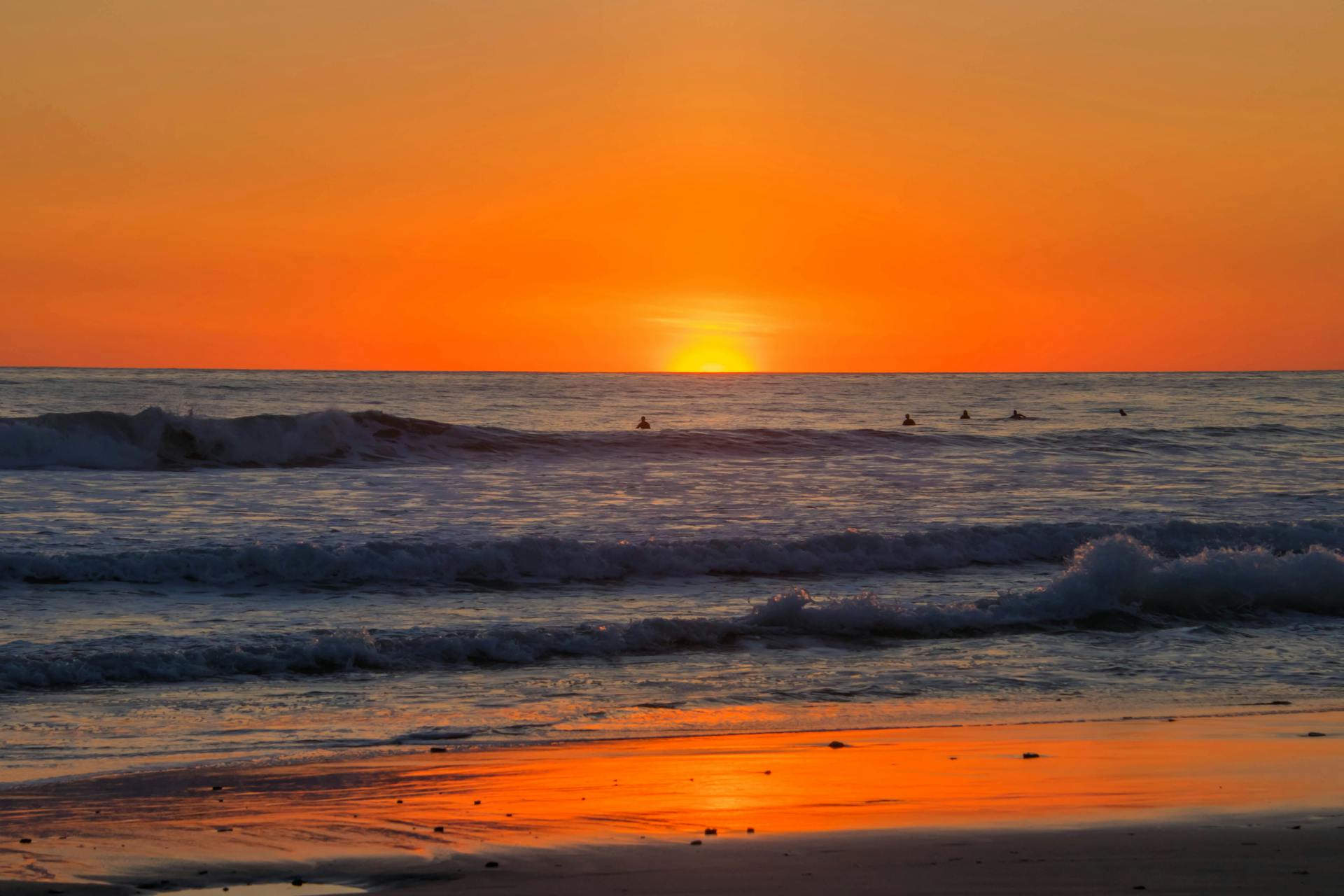 Beautiful sunset over a serene beach in Puntarenas, Costa Rica with waves and surfers in view.