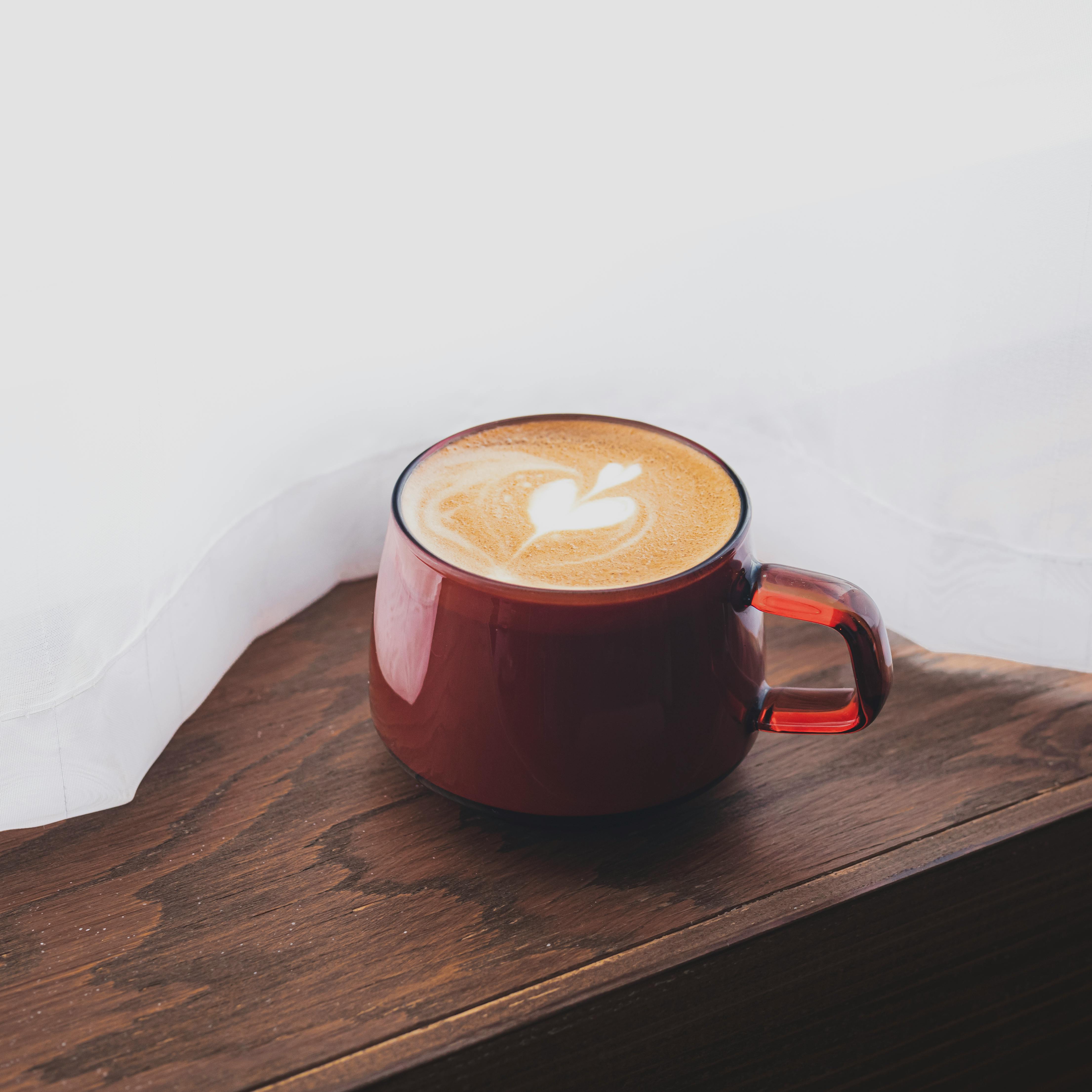 A beautiful latte with heart-shaped latte art in a red mug on a wooden surface.