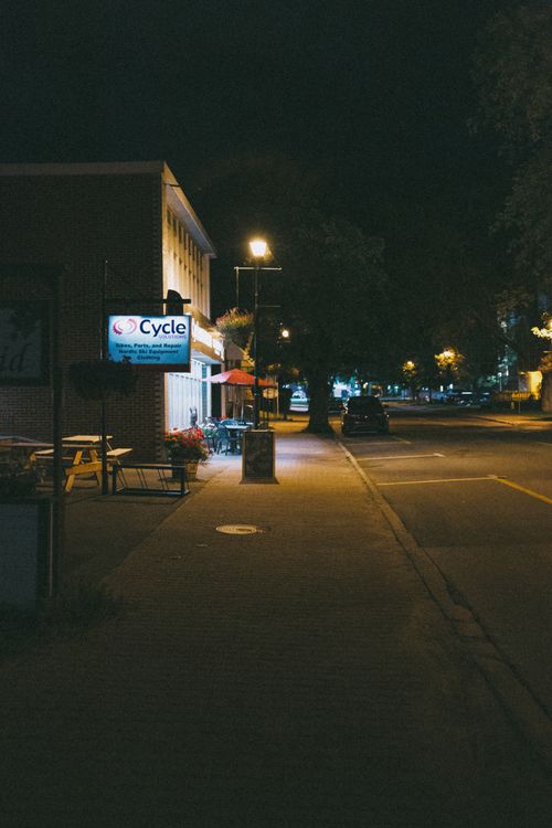 Free Nighttime urban street with parked car and bicycle shop, dimly lit atmosphere captured with artistic flair. Stock Photo