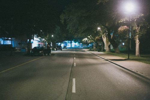 Free A peaceful urban street scene captured at night with cars parked and streetlights illuminating the road. Stock Photo