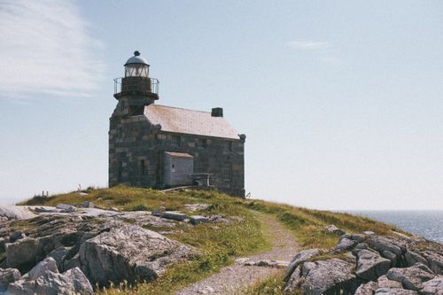 Free Charming lighthouse on a rocky coastal hill with scenic blue sky and sea views. Stock Photo