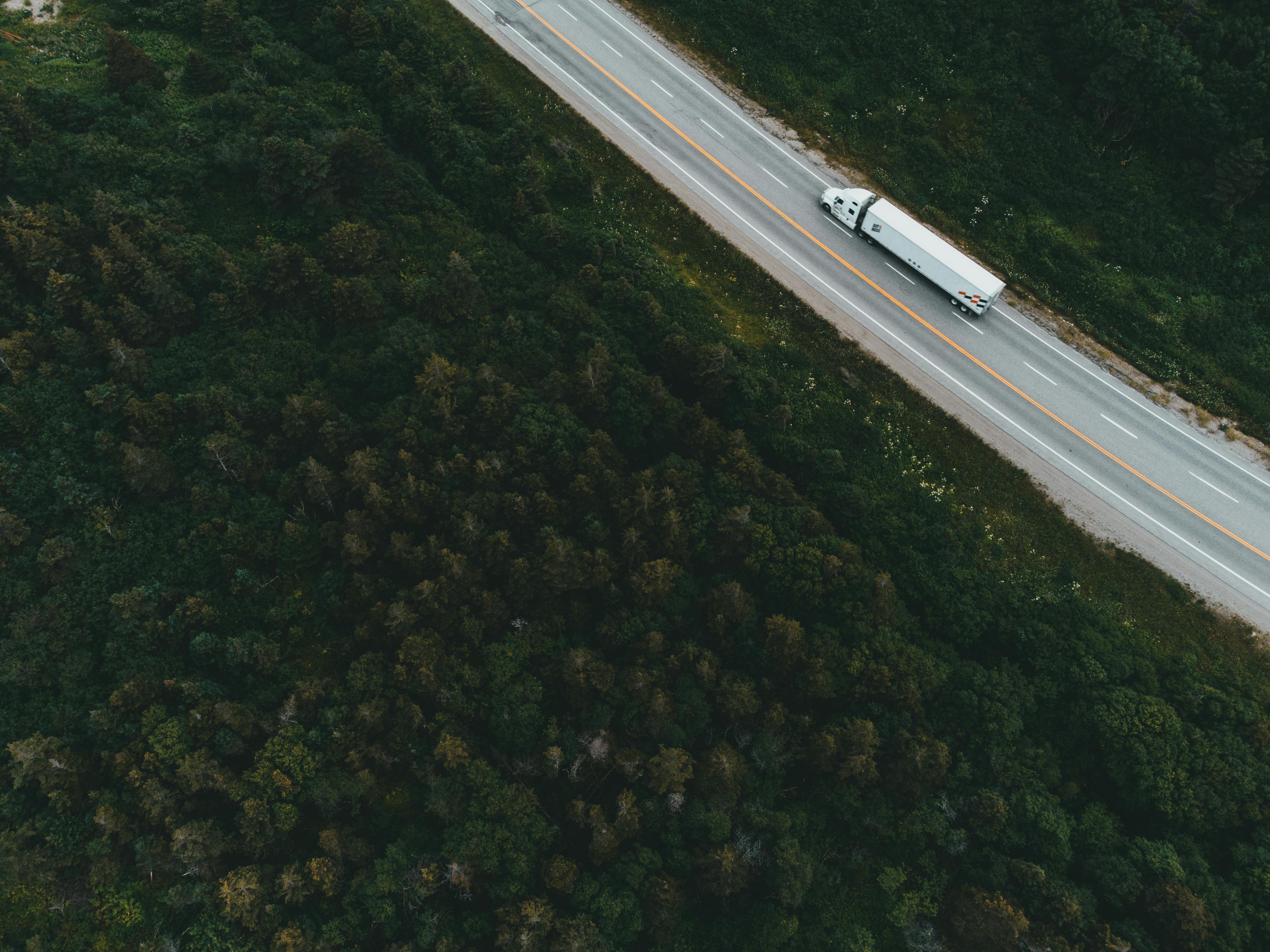 Aerial drone shot of container truck driving through forested highway representing FieldBase last-mile logistics