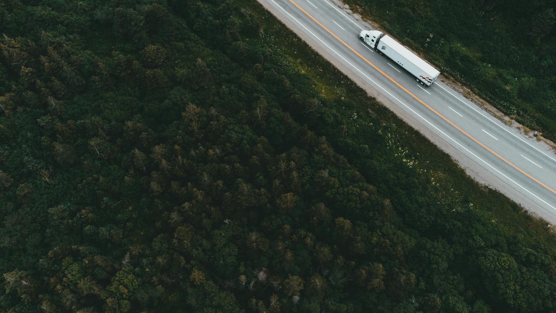 Aerial drone shot of container truck driving through forested highway representing FieldBase last-mile logistics
