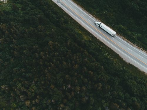 Free Drone shot of a container truck traveling on a forested highway during the day. Stock Photo