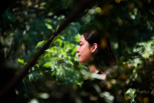 Side profile of a woman surrounded by lush green foliage in a serene garden setting.