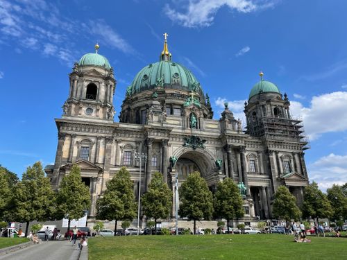 Free Low angle view of Berlin Cathedral against a bright blue sky, framed by lush green trees. Stock Photo