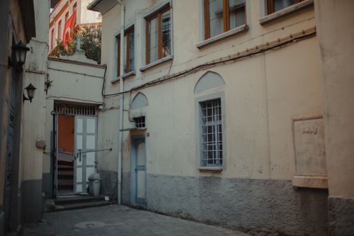 Free Scenic narrow alley with pastel buildings, featuring windows, doors, and a flag in a tranquil urban setting. Stock Photo