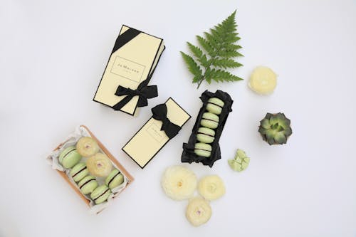 Boxes of Perfumes Beside Macaroons on Surface with Fern Leaf and Flowers