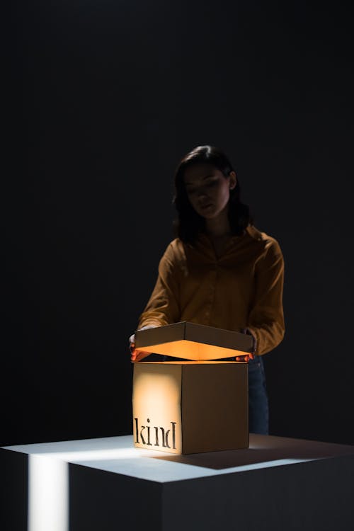 Young ethnic woman opening cardboard box standing on table