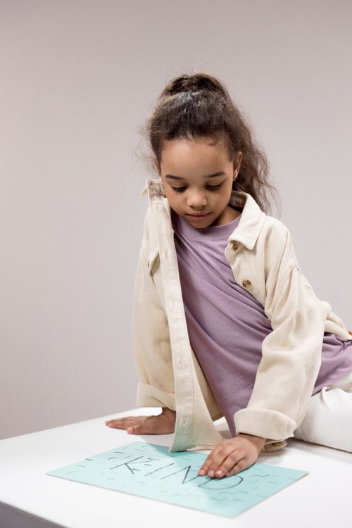 Free Adorable girl sitting indoors, focused on a creative task with a kind message. Stock Photo