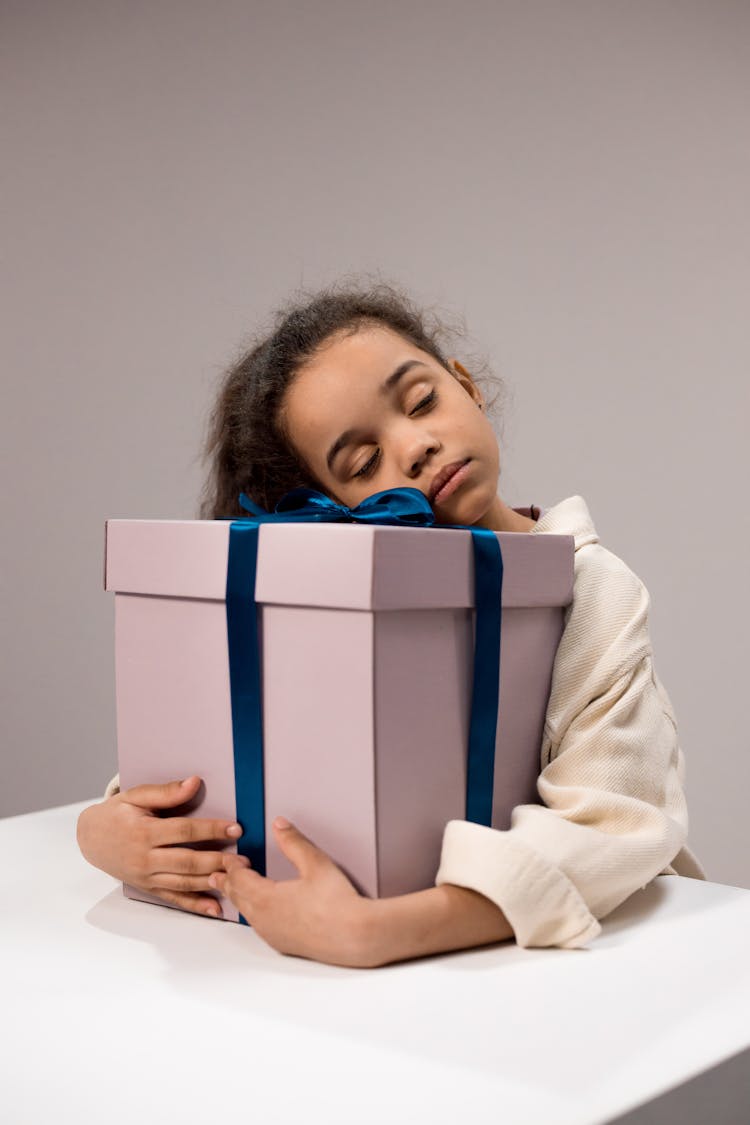 Photograph Of A Girl Holding A Gift Box While Her Eyes Are Closed