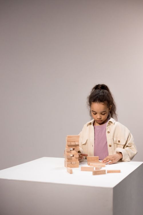 Free Young girl playing with a tower of wooden blocks, focused and concentrated indoors. Stock Photo