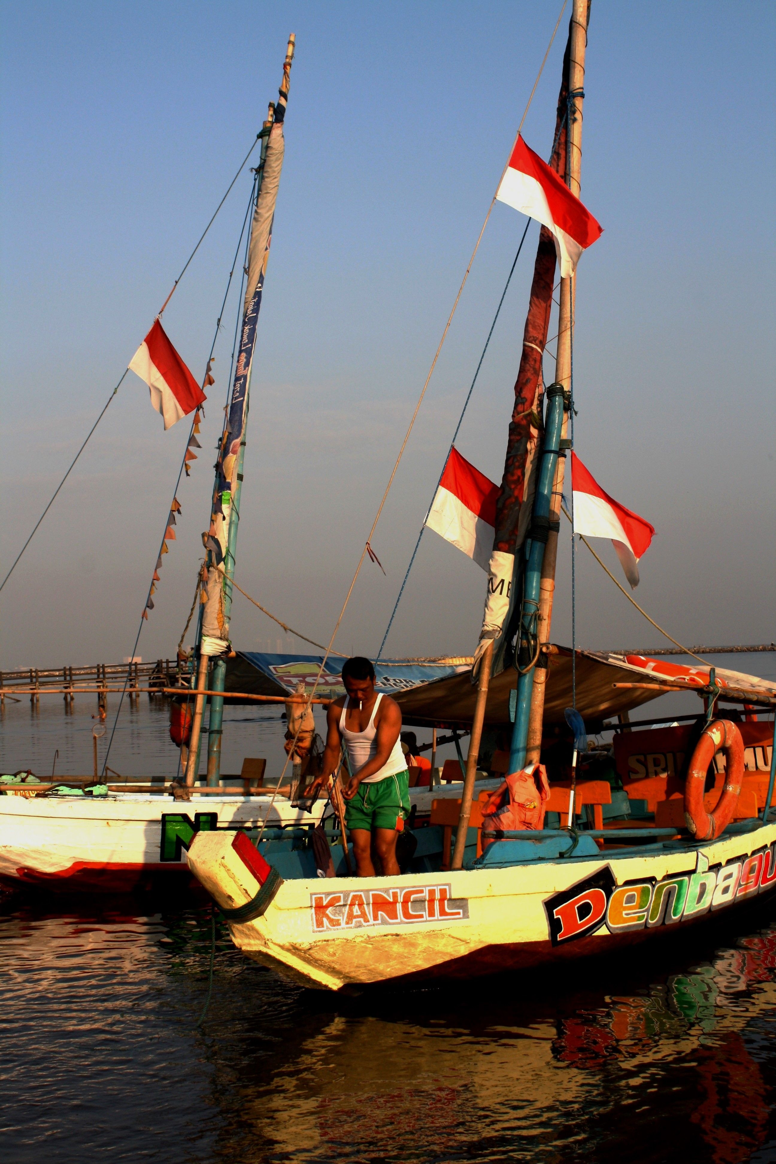 Traditional Indonesian boats docked at sunset, with a man preparing for departure, reflecting cultural heritage.