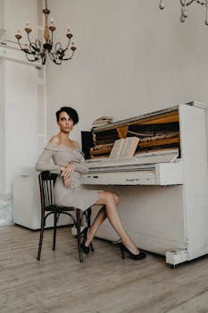 Sophisticated woman in off-shoulder dress sits by an open, rustic piano in a classic, vintage room.