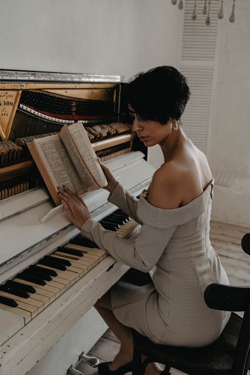 A Woman in a Dress Holding a Book in Front of a Piano