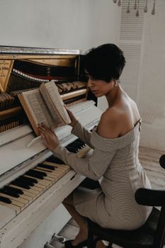 A stylish woman in an off-shoulder dress reading a book while seated at an open piano.