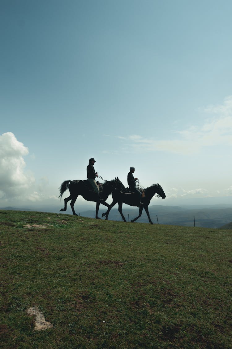 Silhouettes Of People Riding Horses On Hill